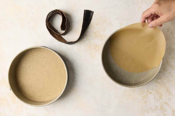 A person lining two cake pans with parchment paper rounds.
