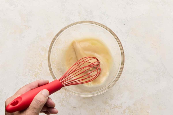 A person whisking egg whites and vanilla in a glass bowl.