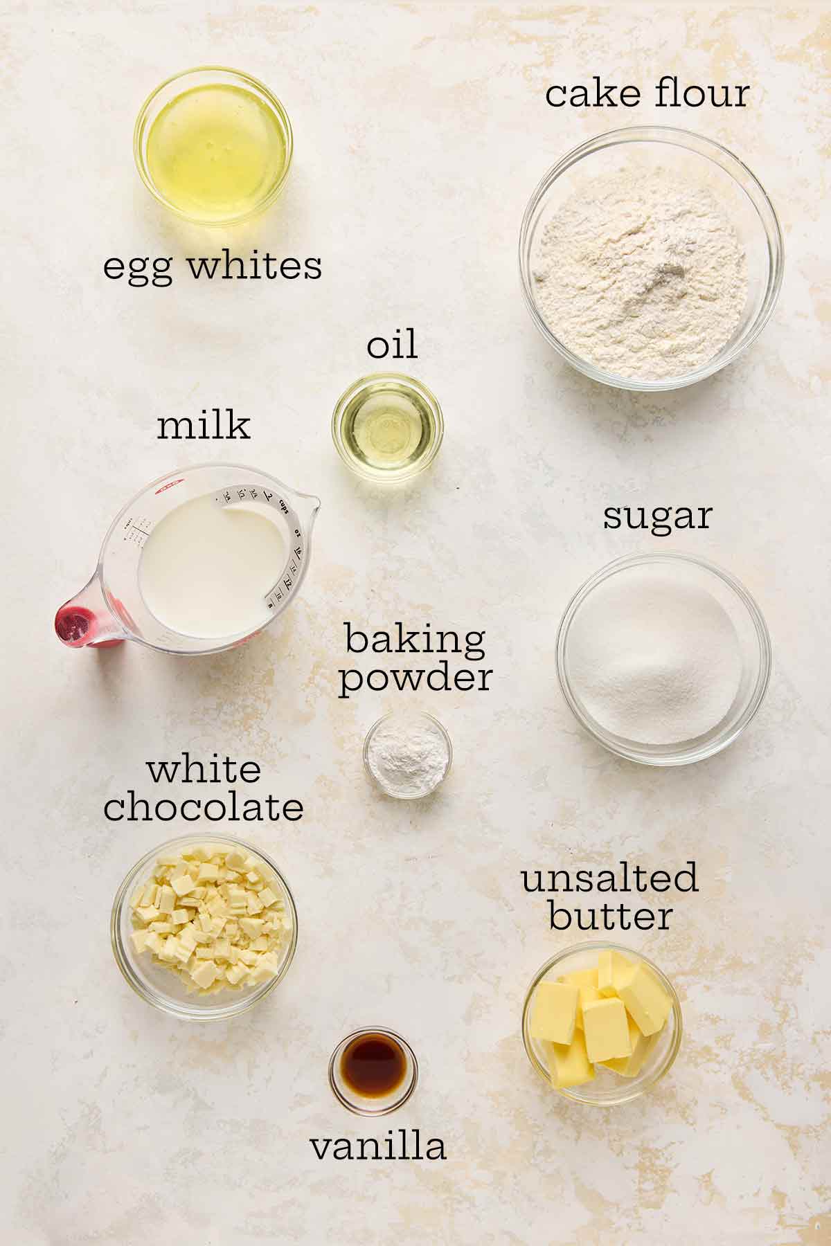 Ingredients for white chocolate whisper cake--egg whites, flour, oil, milk, butter, sugar, baking powder, white chocolate, and vanilla.