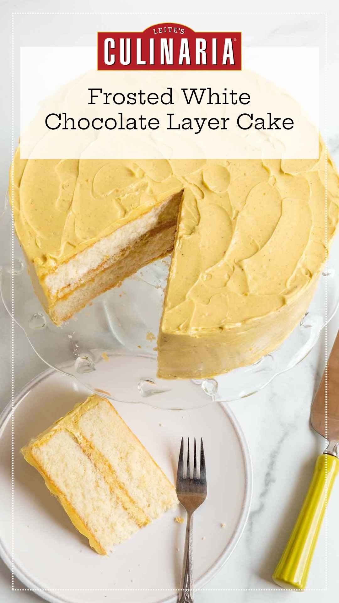 A frosted two layer white chocolate cake on a cake stand with one slice cut from it on a plate nearby.