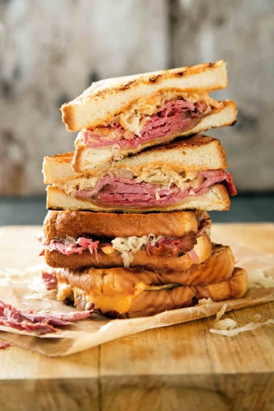 Quartered sections of a reuben sandwich stacked on top of each other on a wooden cutting board.