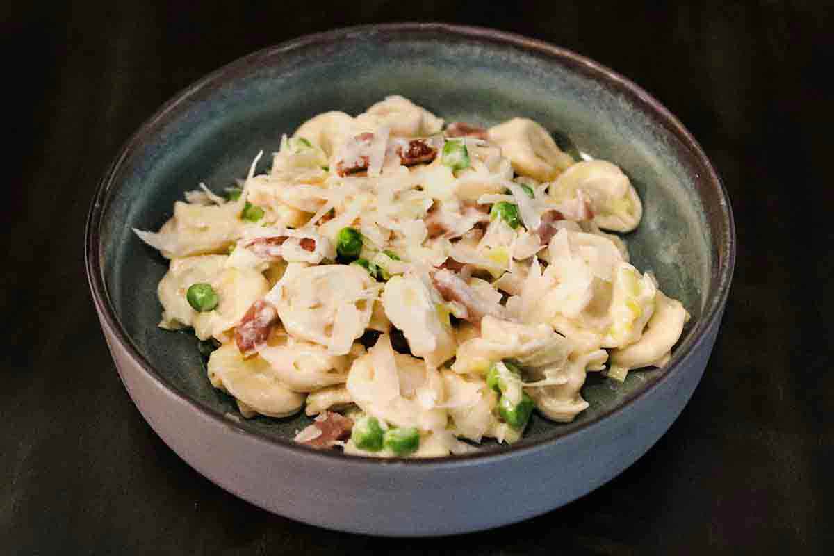 A bowl of tortellini with prosciutto and peas in a cream sauce.