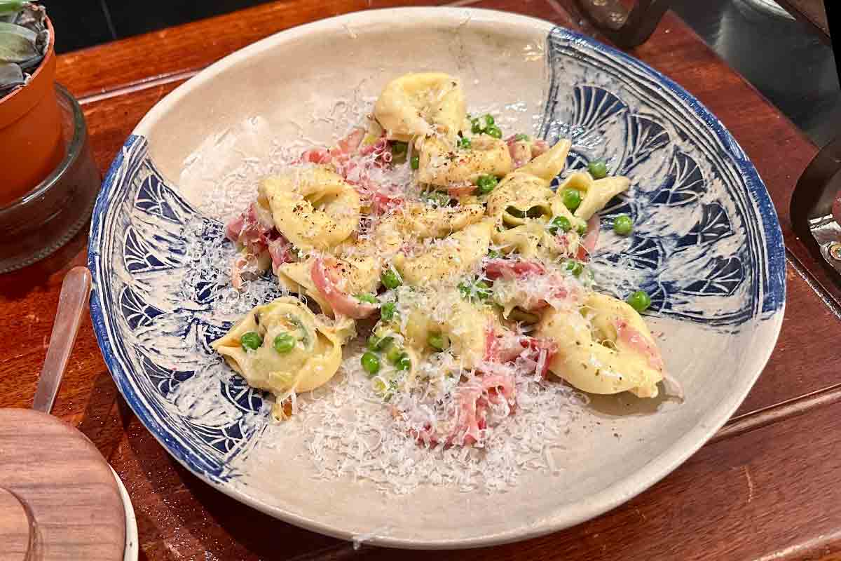 A shallow serving bowl with a serving of tortellini with prosciutto and peas topped with grated Parmesan.