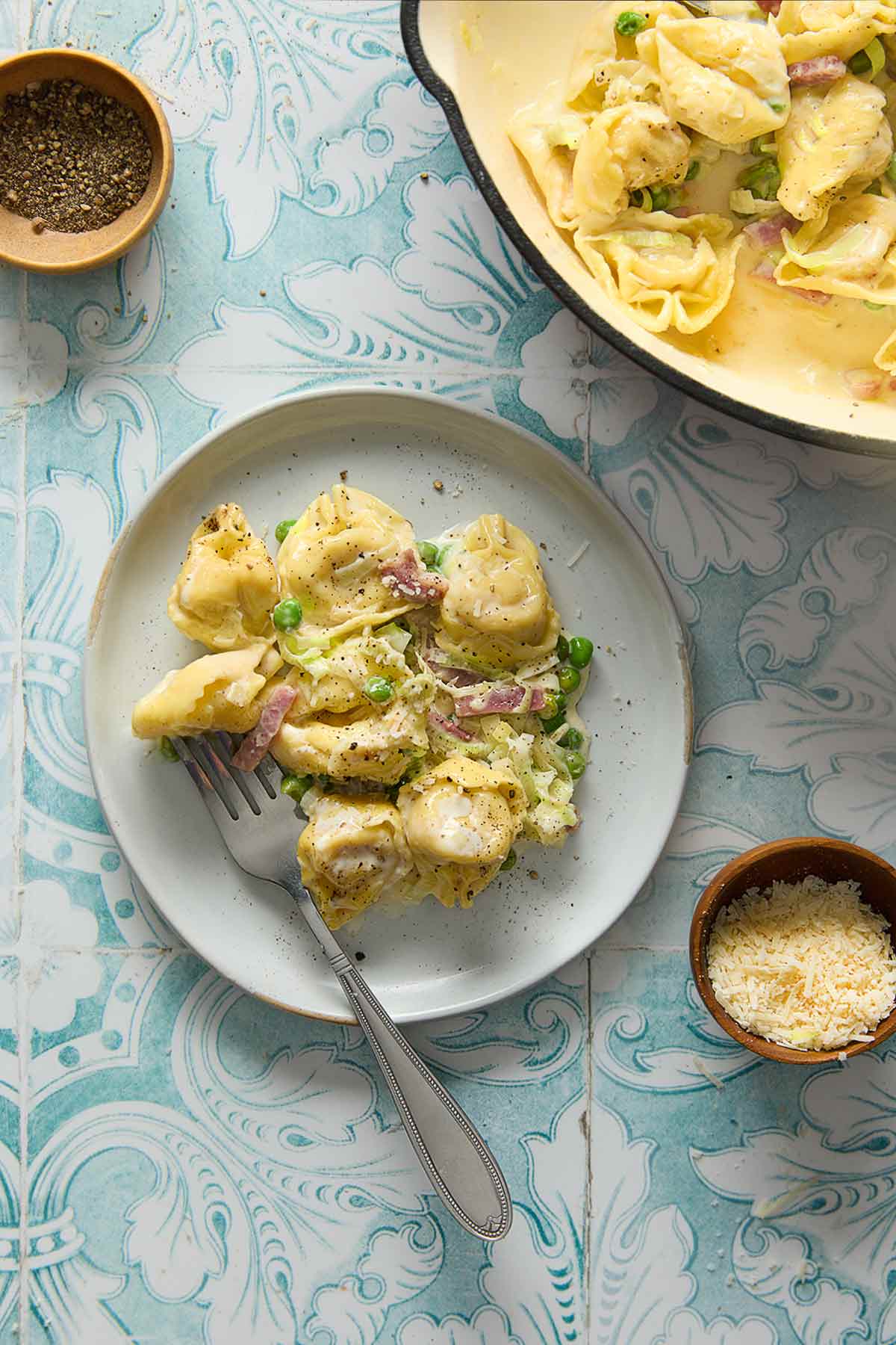 A serving of one-pot tortellini on a plate with a skillet with the remainder nearby.