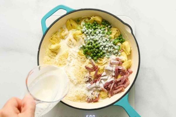 Tortellini, peas, cheese, and prosciutto being combined in a skillet.