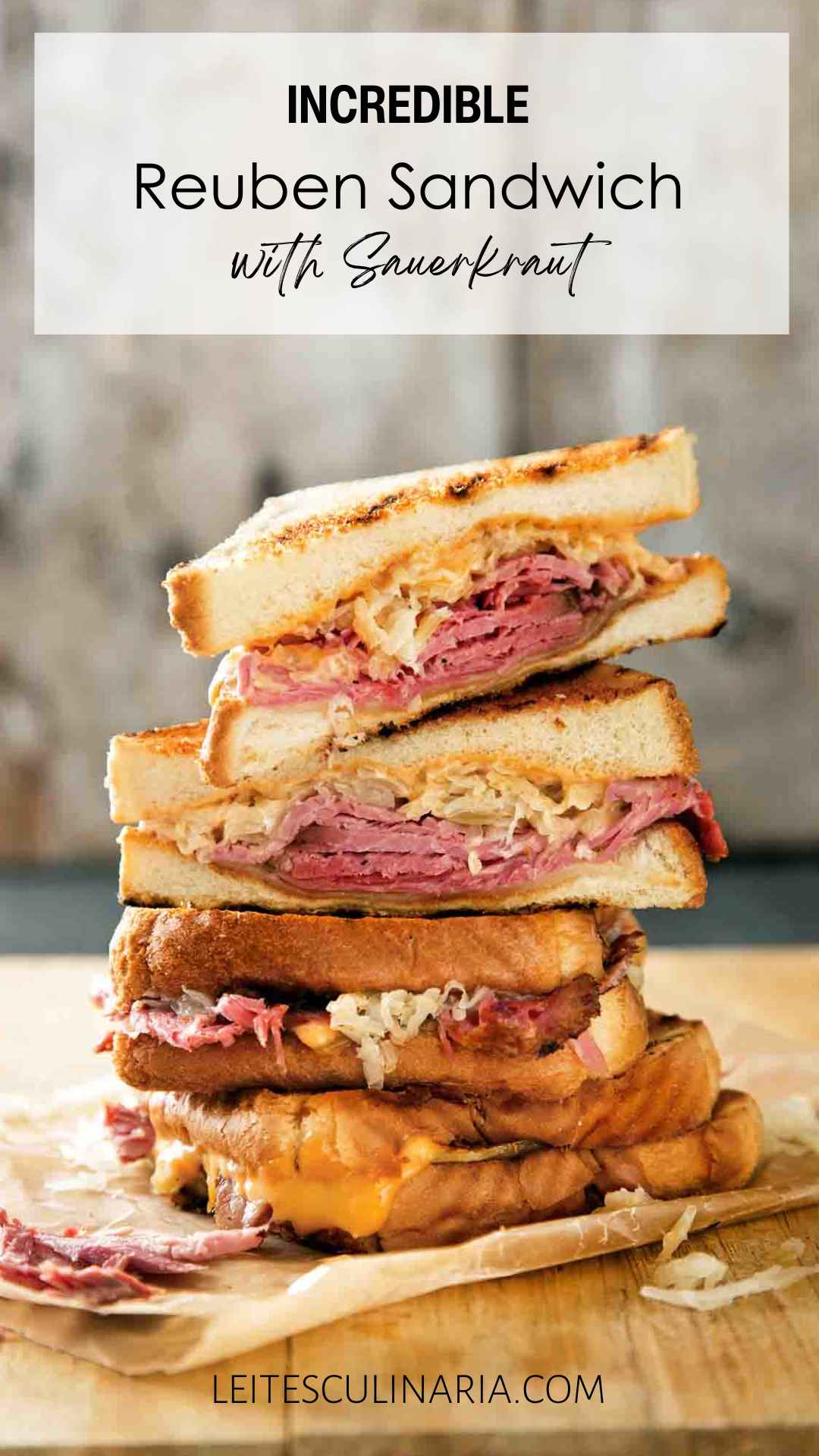 Quartered sections of a reuben sandwich stacked on top of each other on a wooden cutting board.