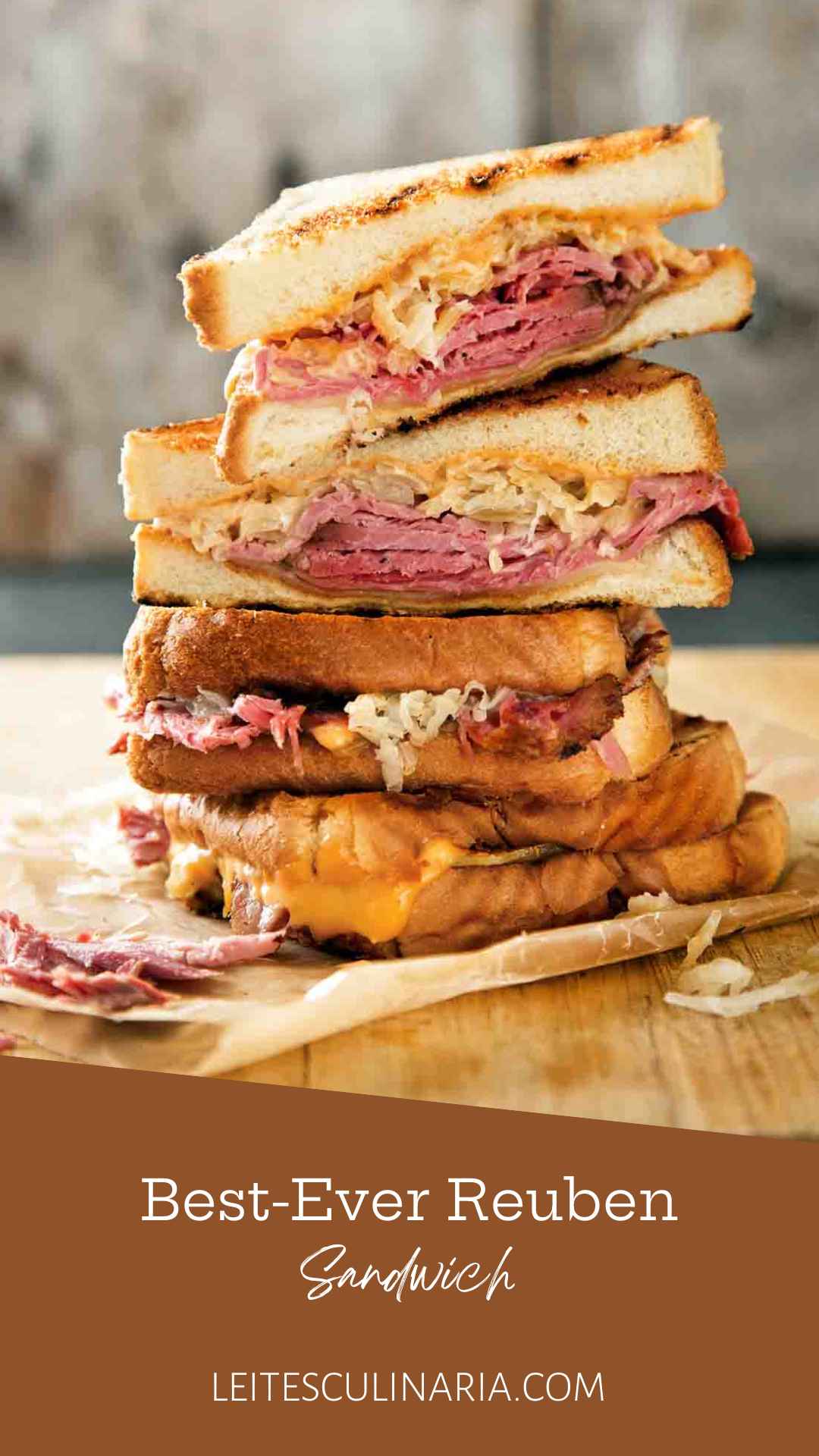 Quartered sections of a reuben sandwich stacked on top of each other on a wooden cutting board.