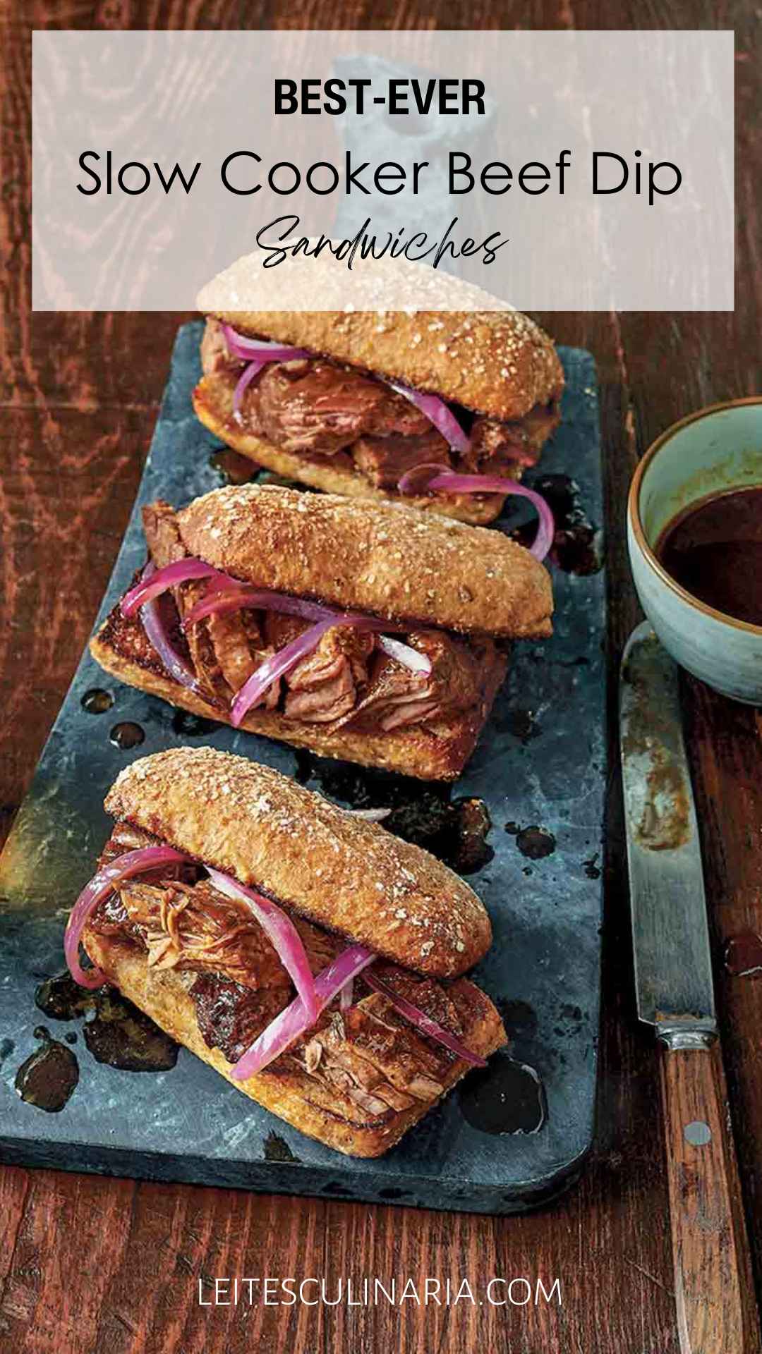 Three slow cooker French dip sandwiches with onions on serving platter with au jus on the side.