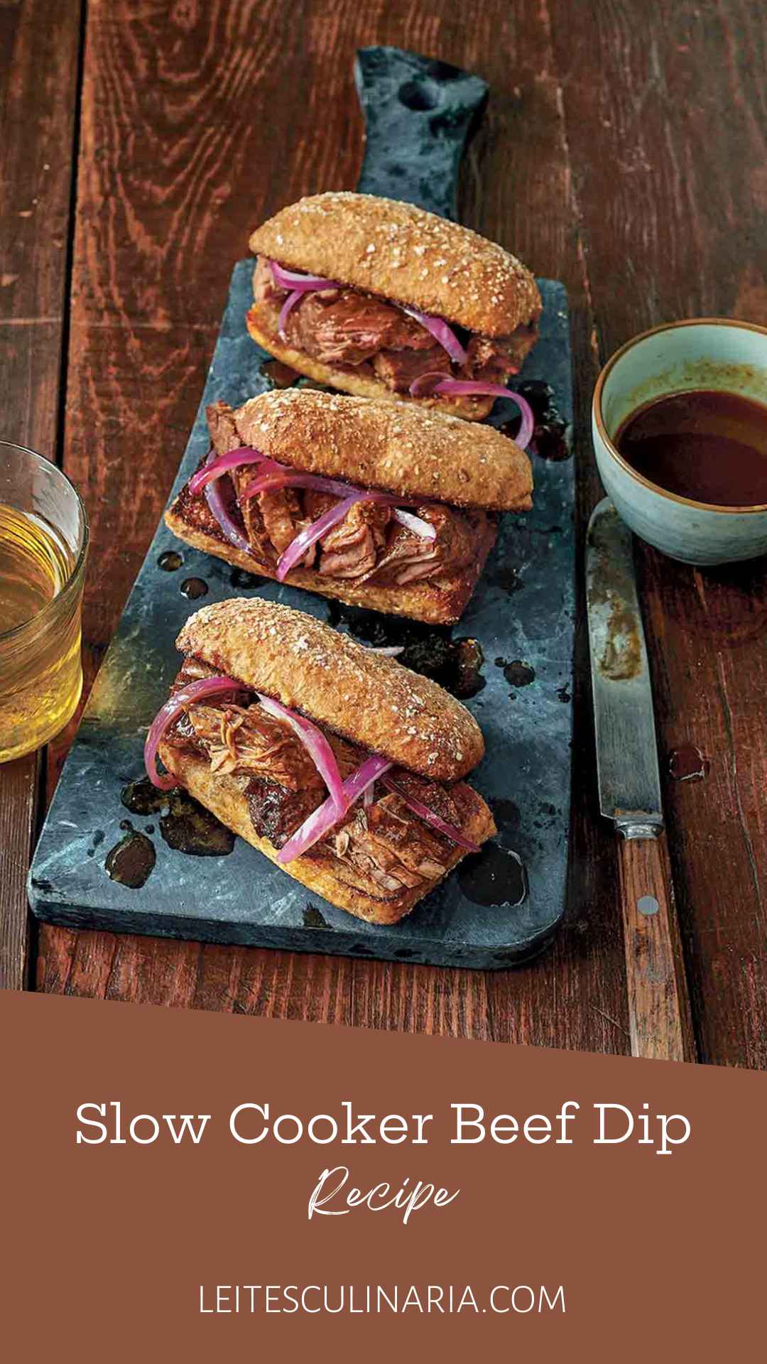 Three slow cooker French dip sandwiches with onions on serving platter with au jus on the side.