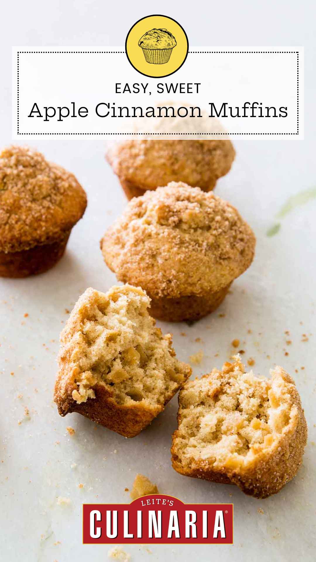 Sugar-topped apple cinnamon muffins on a white counter. The muffin in the forefront is broken in half.