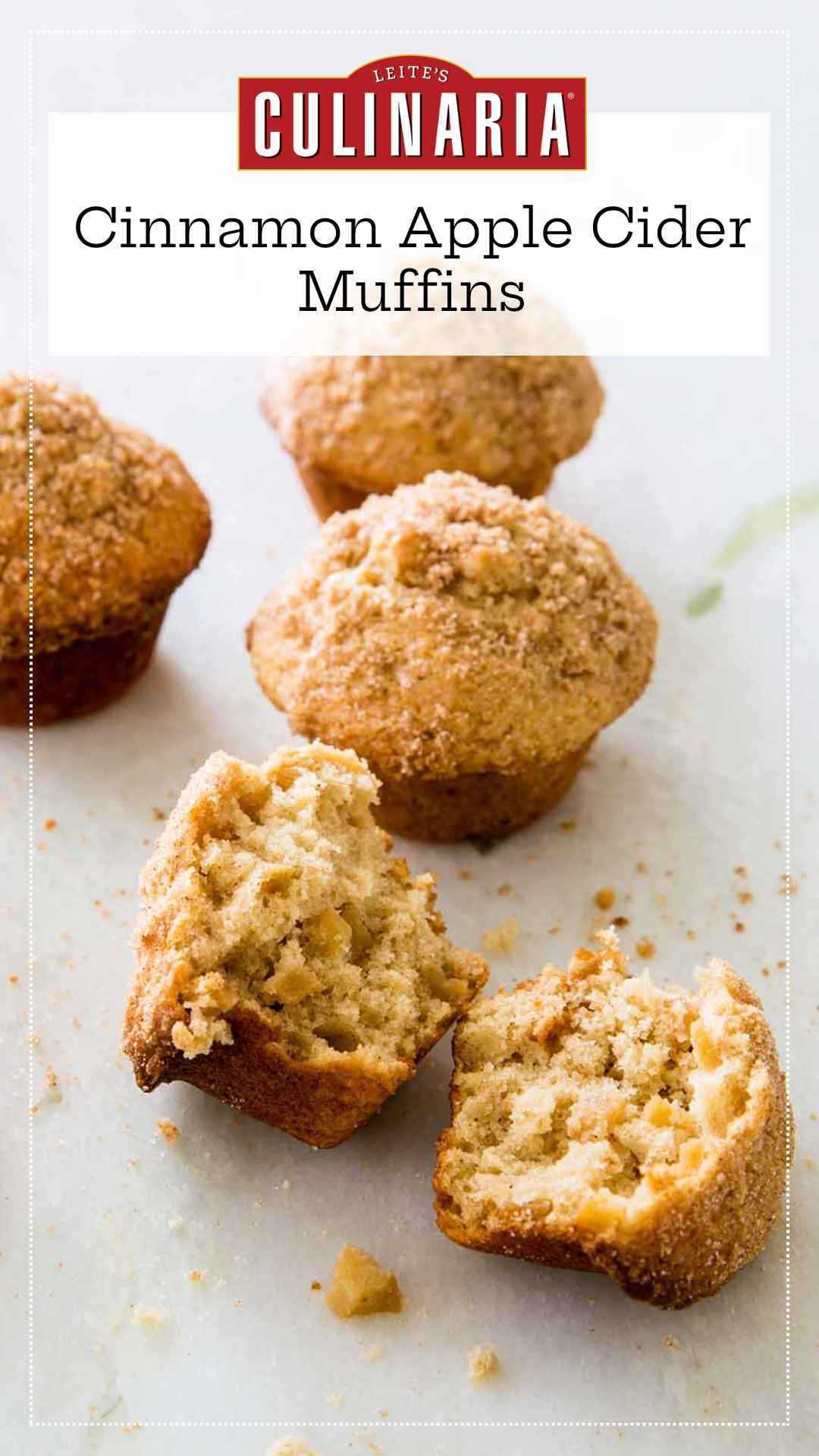 Sugar-topped apple cinnamon muffins on a white counter. The muffin in the forefront is broken in half.