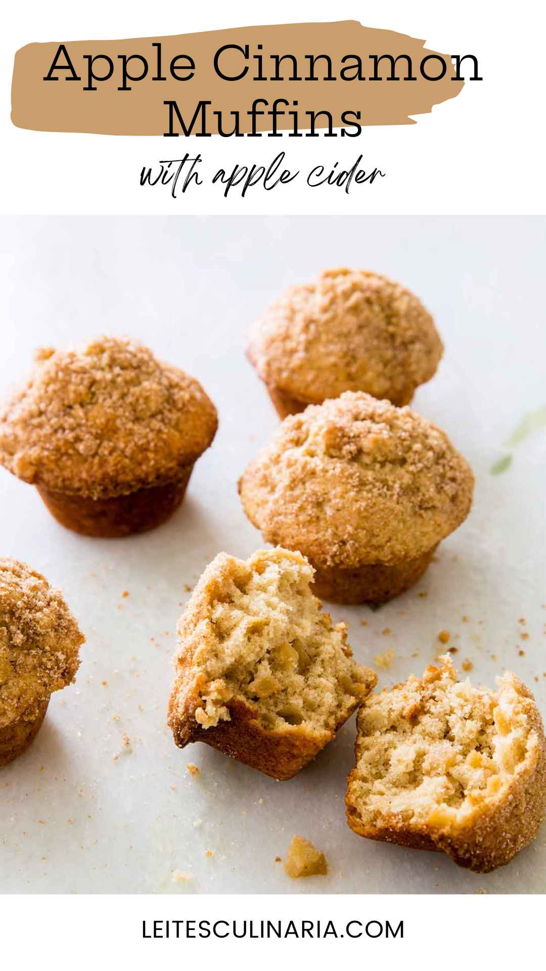 Sugar-topped apple cinnamon muffins on a white counter. The muffin in the forefront is broken in half.