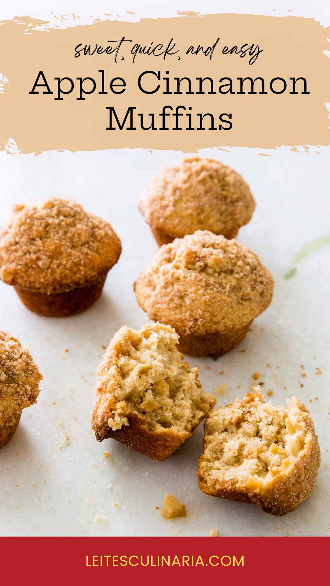 Sugar-topped apple cinnamon muffins on a white counter. The muffin in the forefront is broken in half.