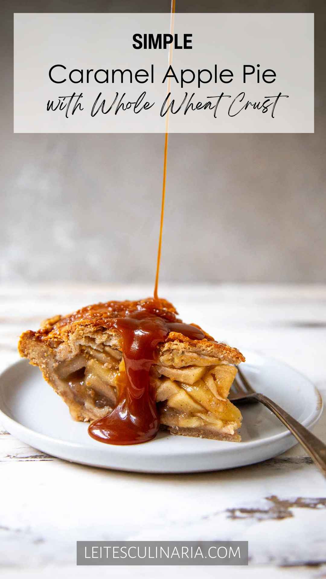 A slice of homemade caramel apple pie on a white plate. A thin stream of homemade caramel is drizzling over the top crust of the pie. A fork sits on the right next to the pie.