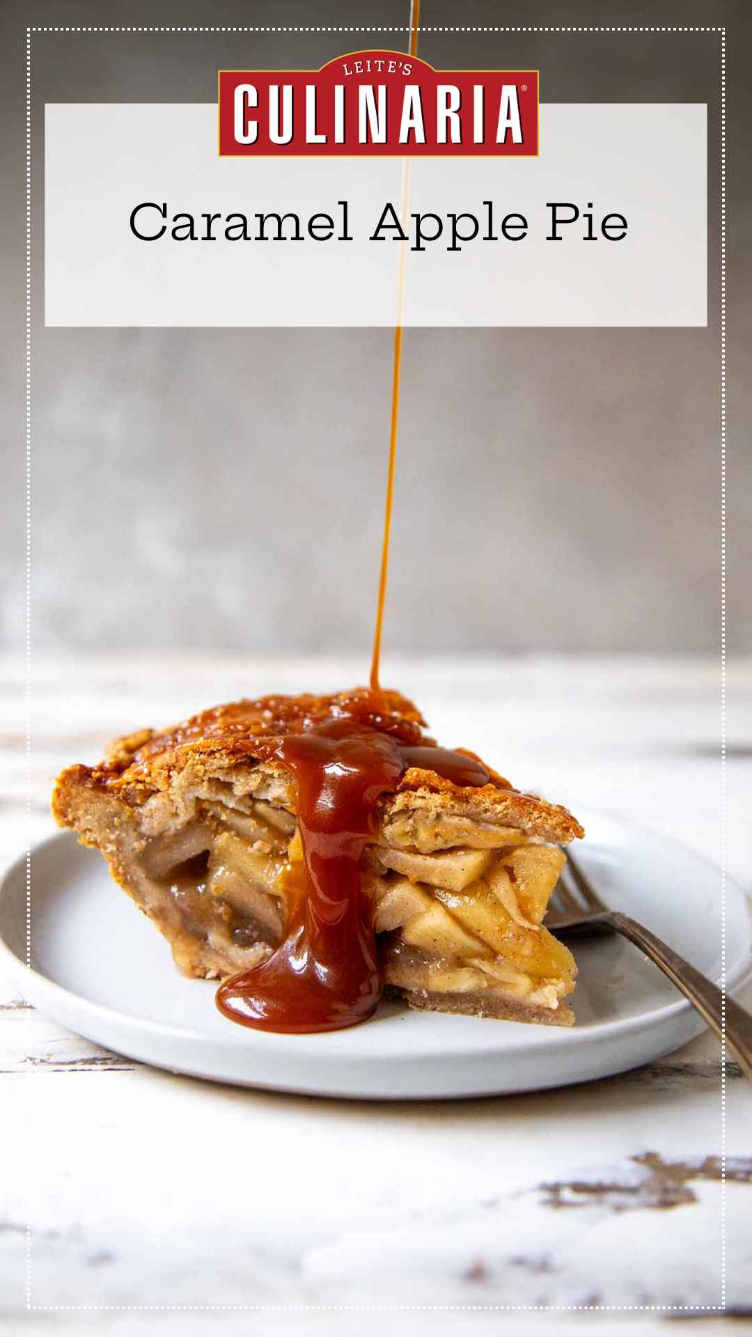 A slice of homemade caramel apple pie on a white plate. A thin stream of homemade caramel is drizzling over the top crust of the pie. A fork sits on the right next to the pie.