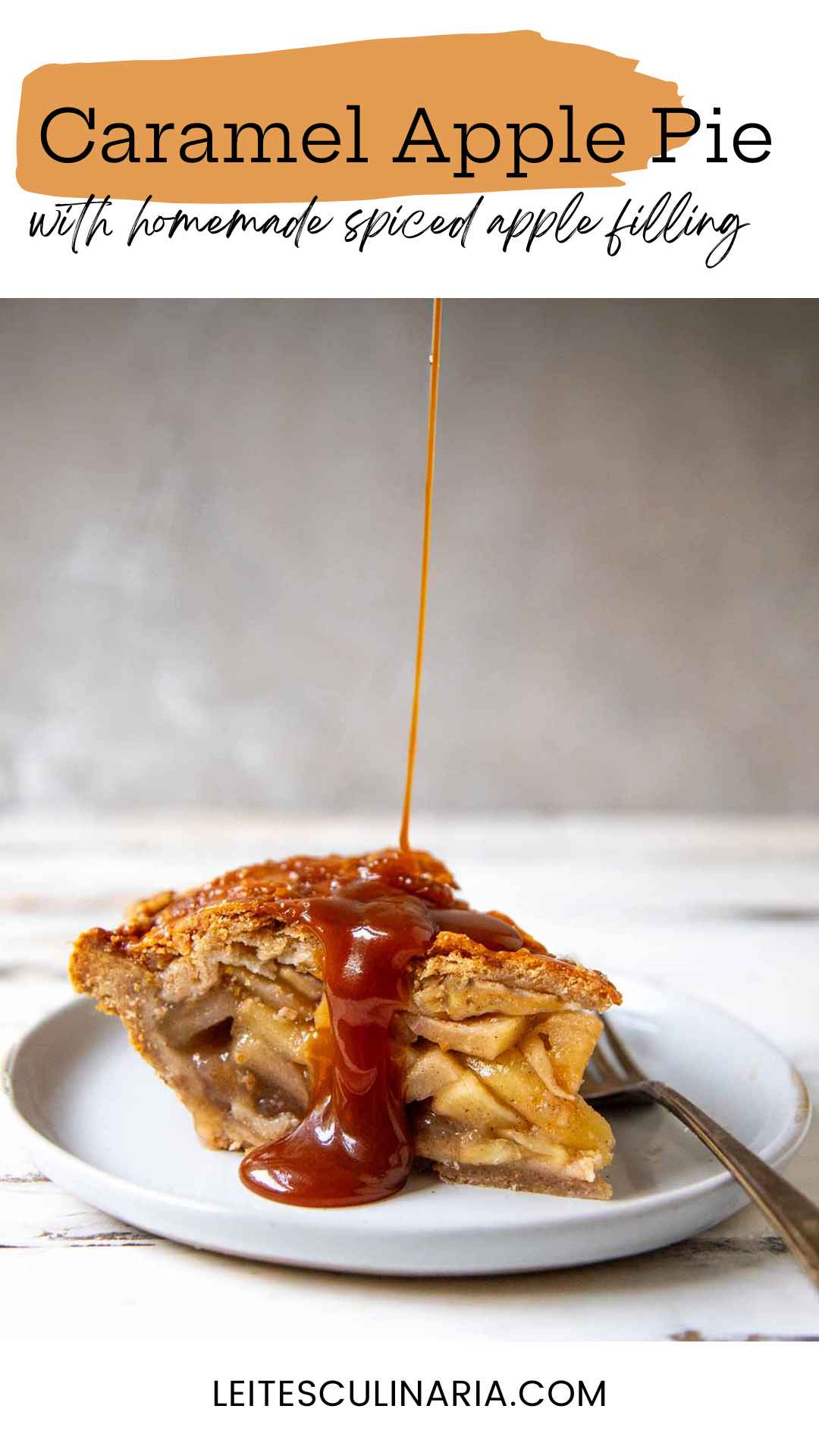 A slice of homemade caramel apple pie on a white plate. A thin stream of homemade caramel is drizzling over the top crust of the pie. A fork sits on the right next to the pie.