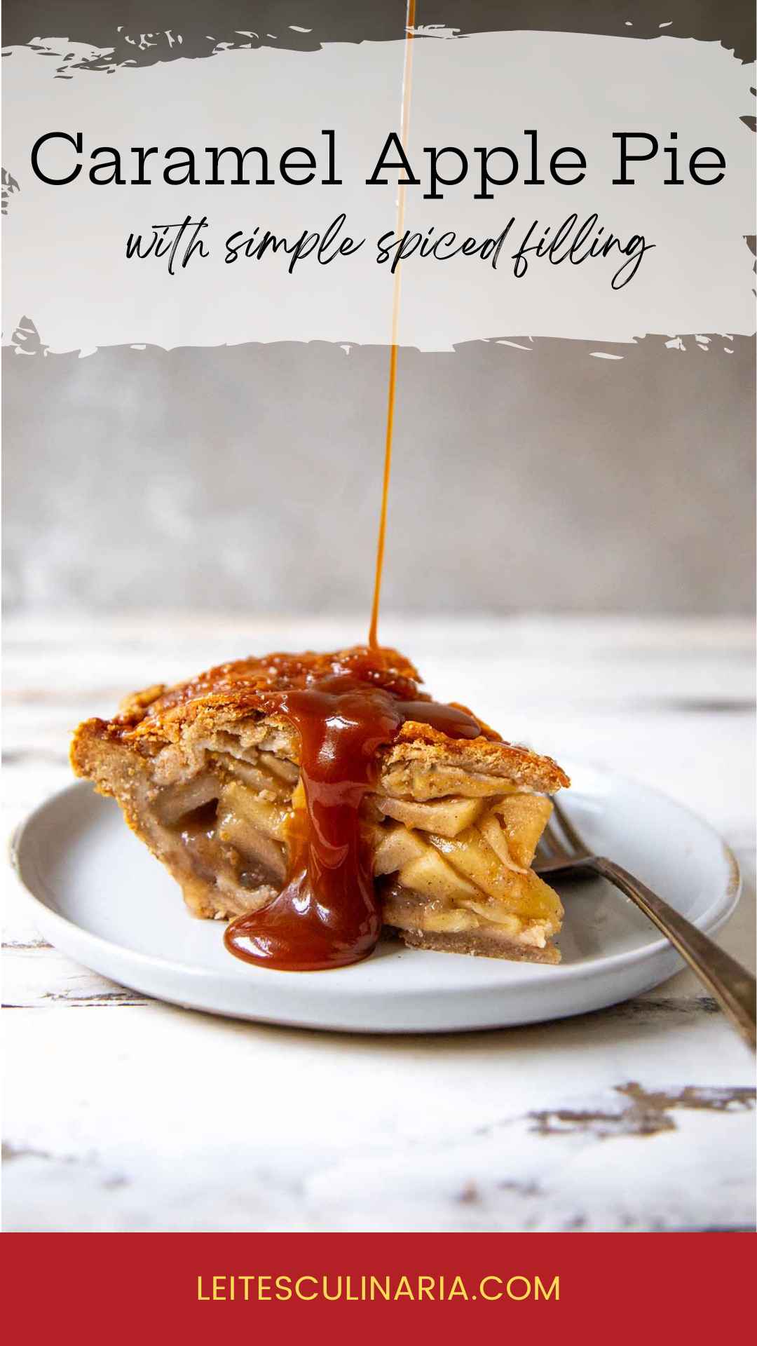 A slice of homemade caramel apple pie on a white plate. A thin stream of homemade caramel is drizzling over the top crust of the pie. A fork sits on the right next to the pie.