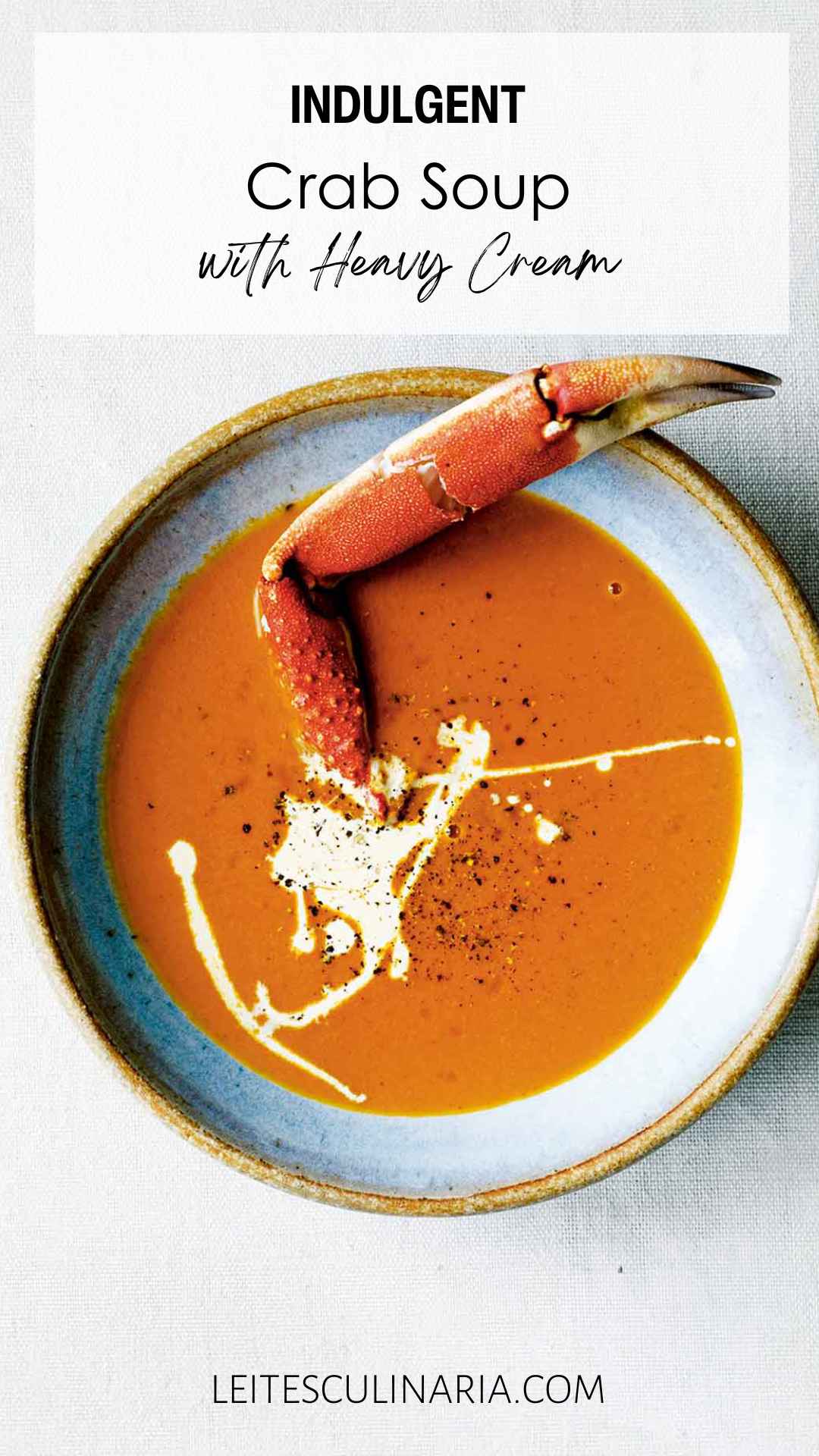 A bowl of crab soup, drizzled with cream, and sprinkled with pepper, with a crab leg sticking out of it.