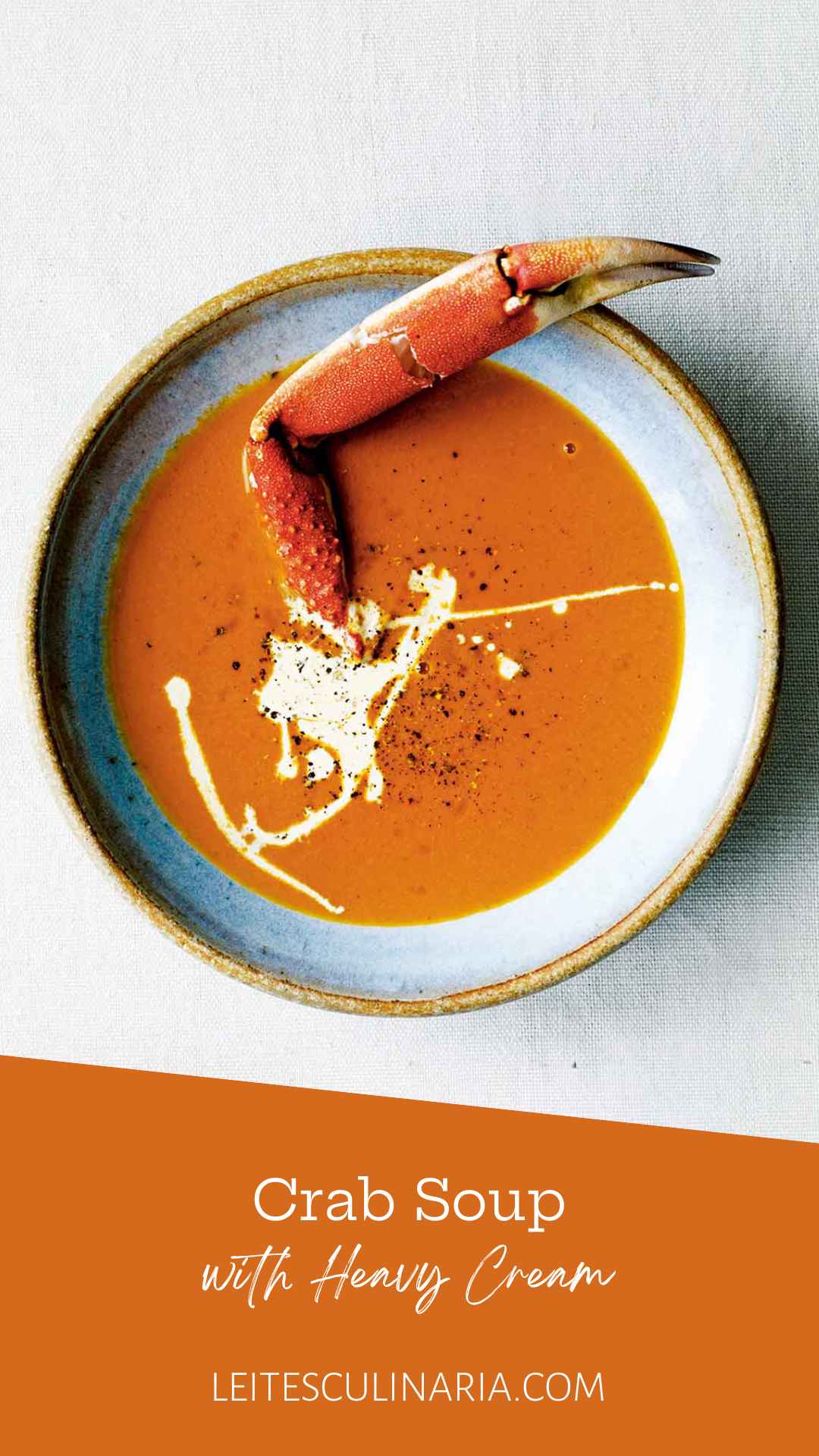 A bowl of crab soup, drizzled with cream, and sprinkled with pepper, with a crab leg sticking out of it.