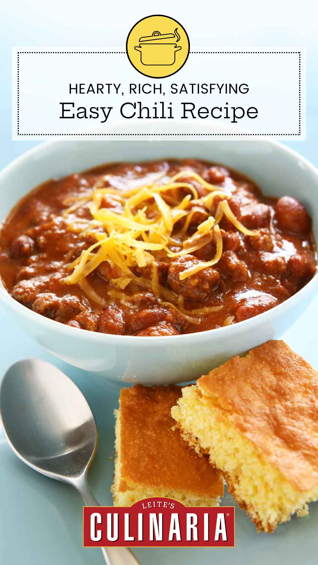 A bowl of chili with shredded cheese on top and two squares of cornbread on the side.