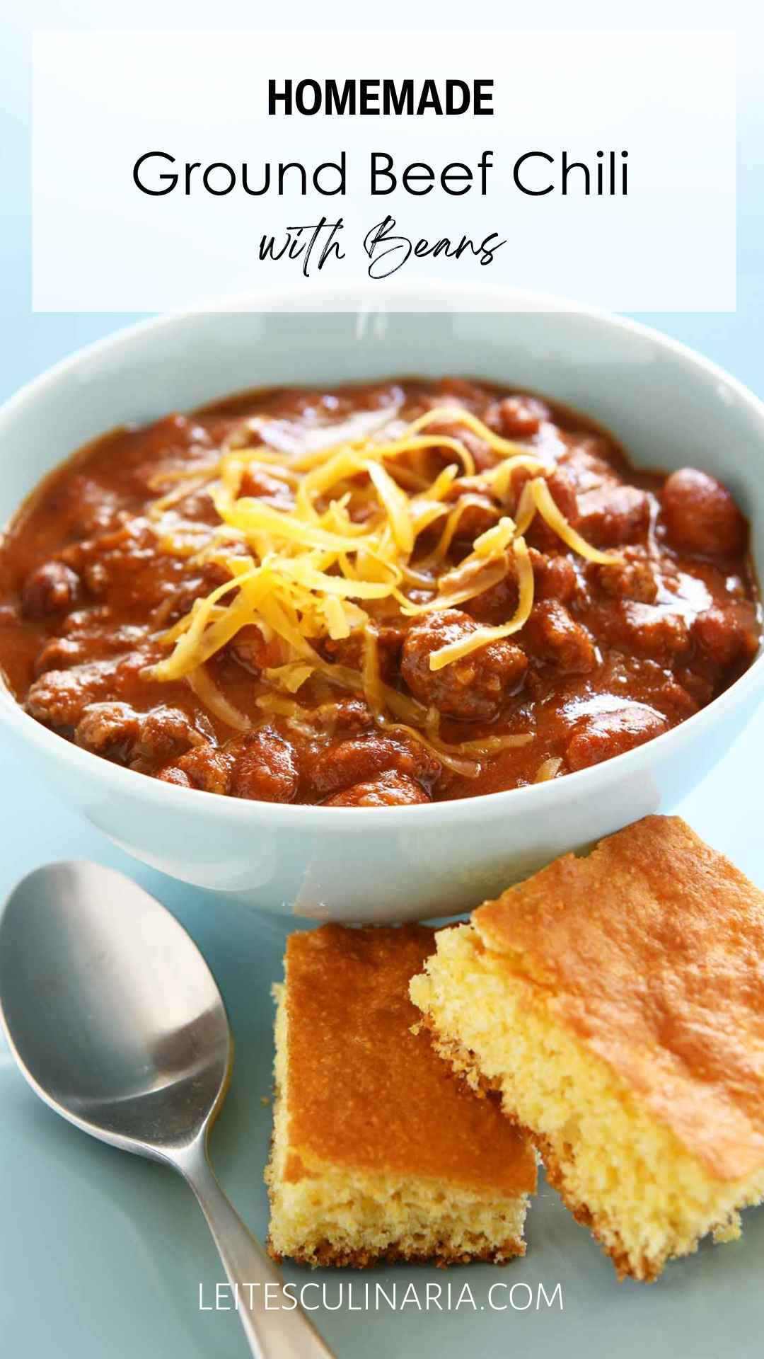 A bowl of chili with shredded cheese on top and two squares of cornbread on the side.