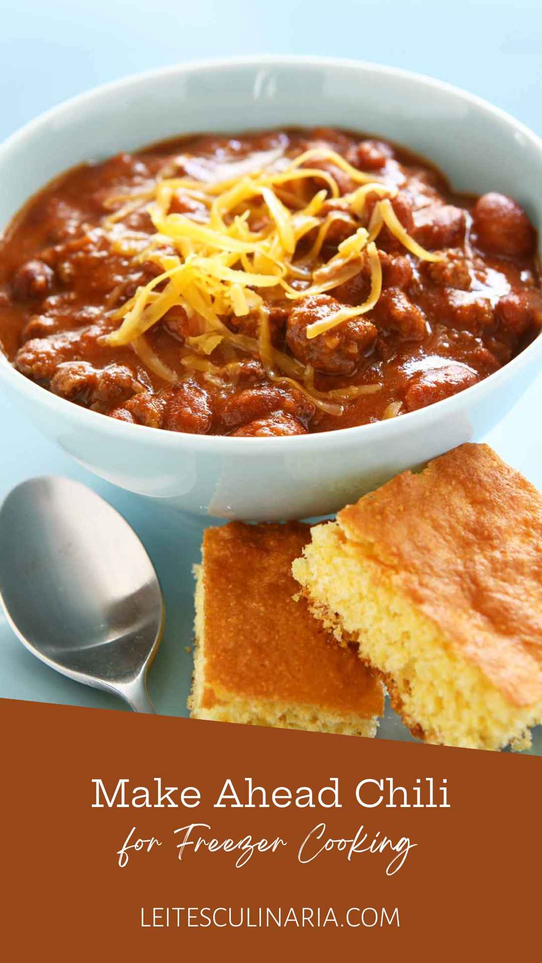 A bowl of chili with shredded cheese on top and two squares of cornbread on the side.