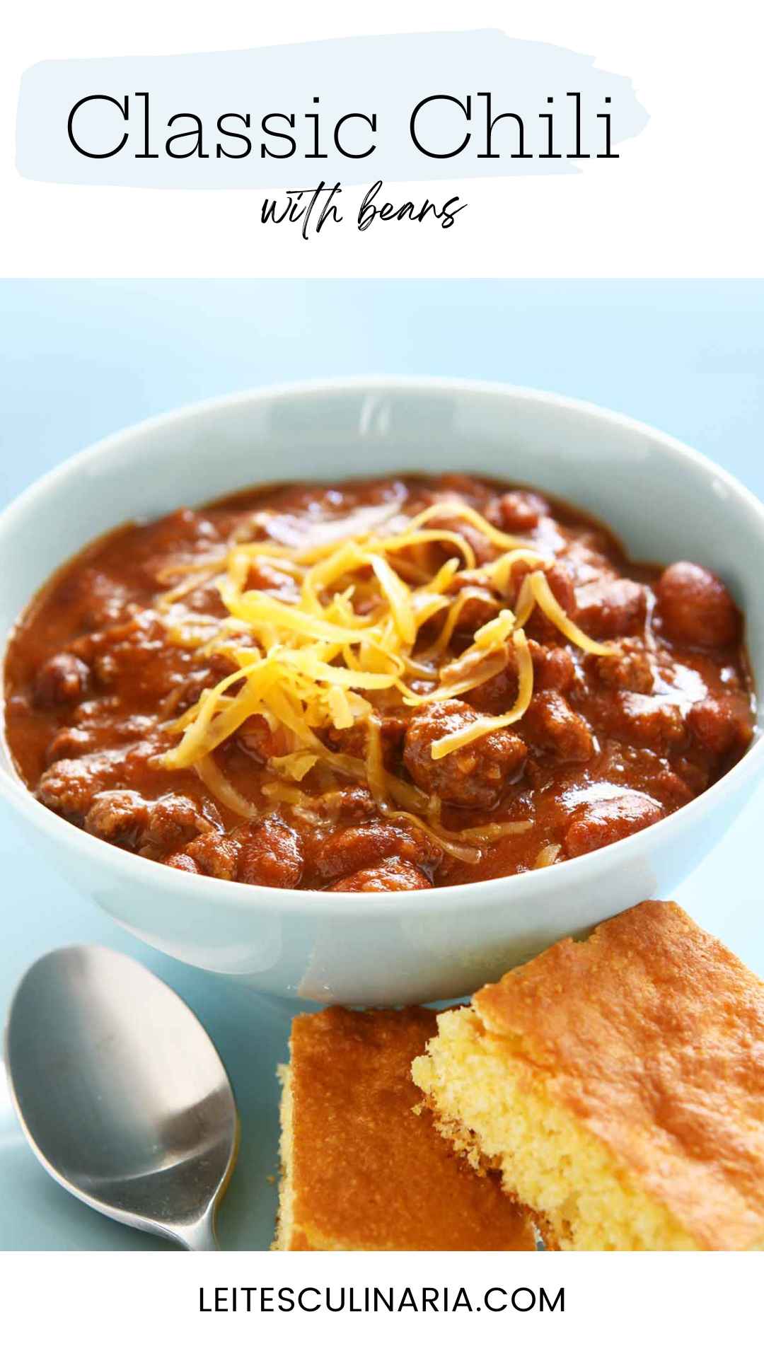 A bowl of chili with shredded cheese on top and two squares of cornbread on the side.