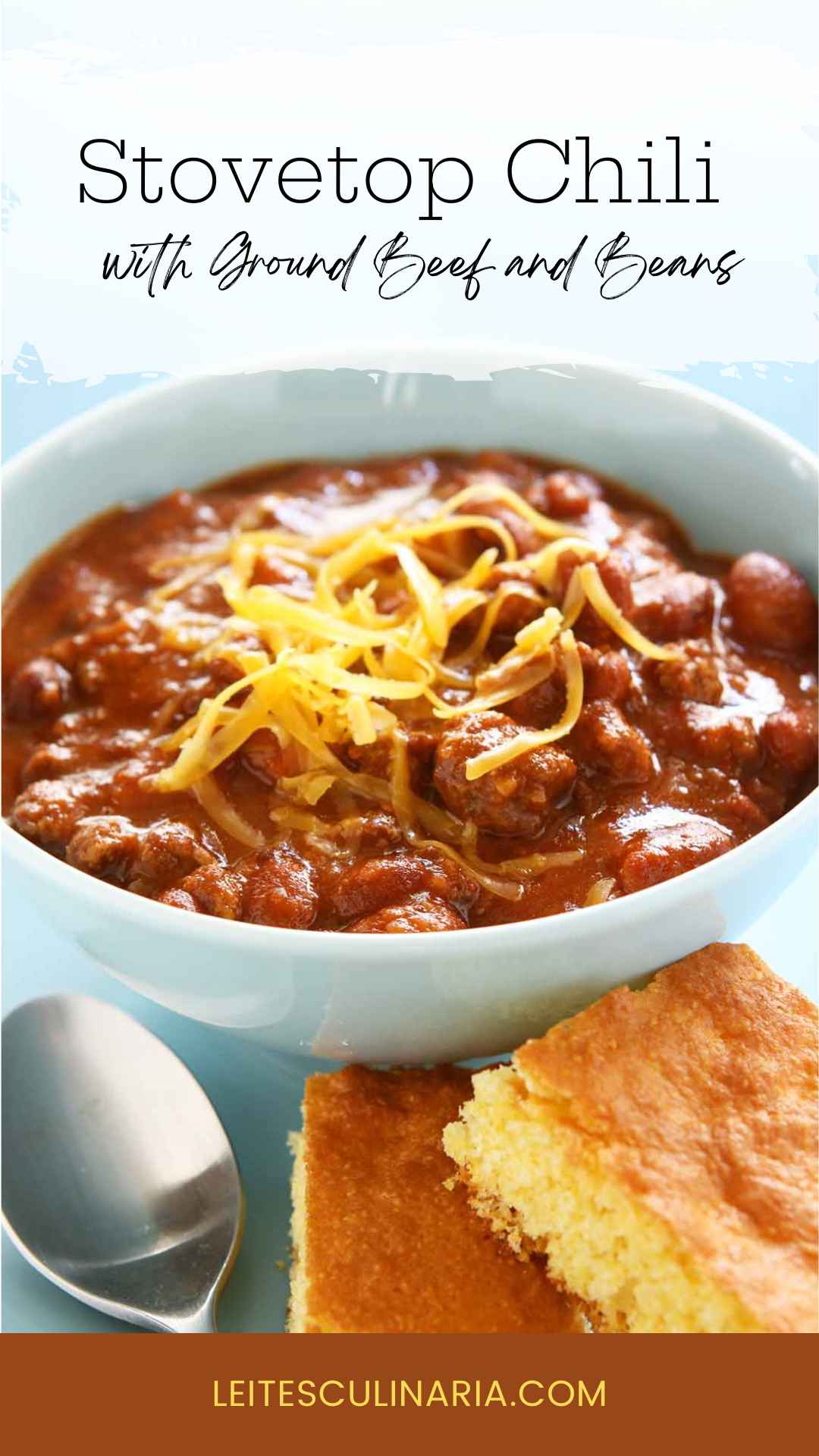 A bowl of chili with shredded cheese on top and two squares of cornbread on the side.