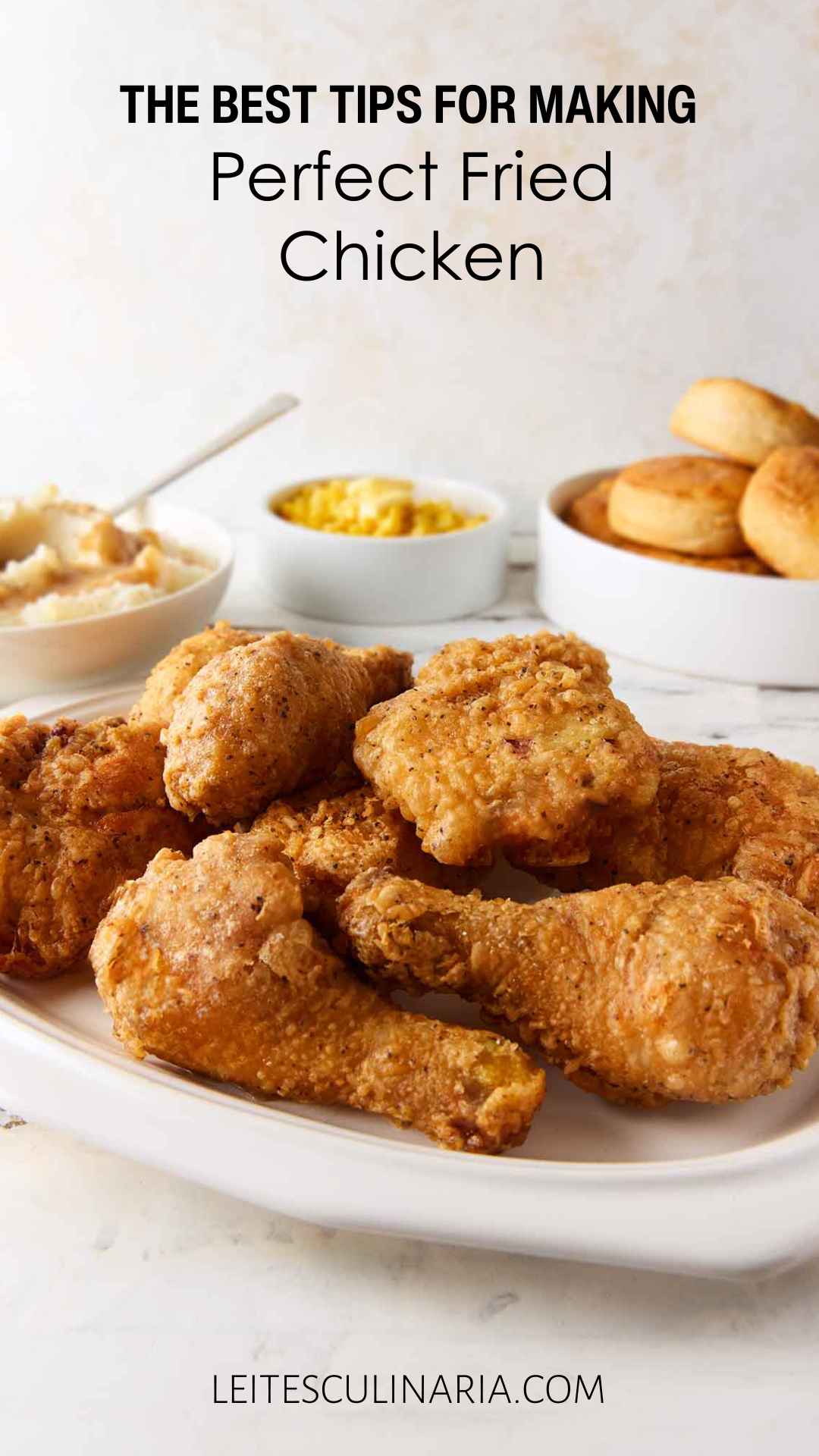 A platter of fried chicken with mashed potatoes, corn, and biscuits in the background.