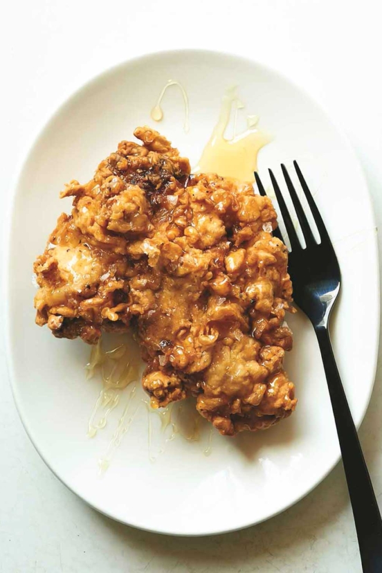 A crispy fried boneless chicken thigh drizzled with honey on a plate with a fork on the side.