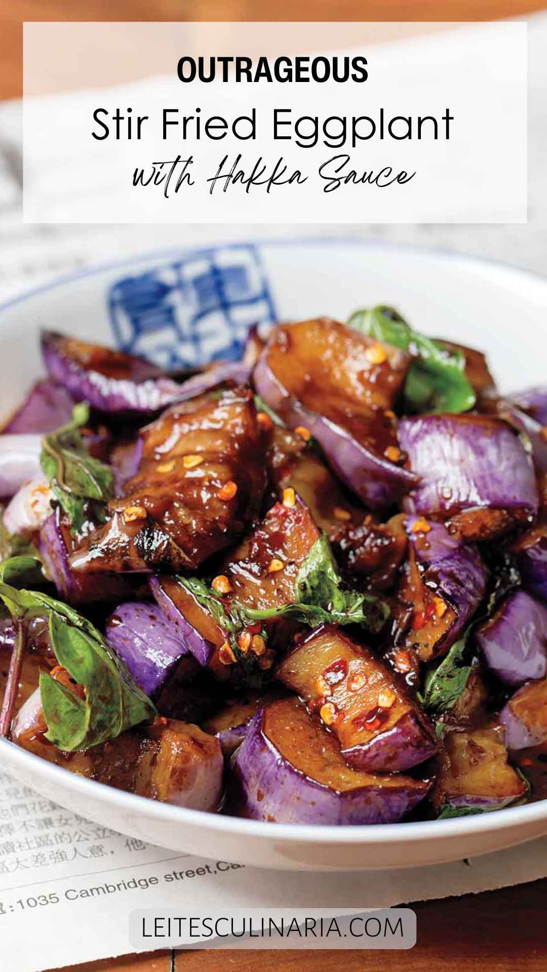 A white bowl filled with stir-fried eggplant in hakka sauce with fresh basil leaves.