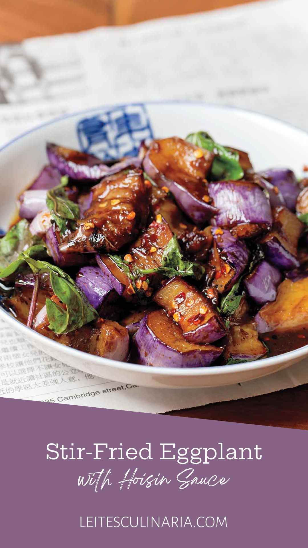 A white bowl filled with stir-fried eggplant in hakka sauce with fresh basil leaves.