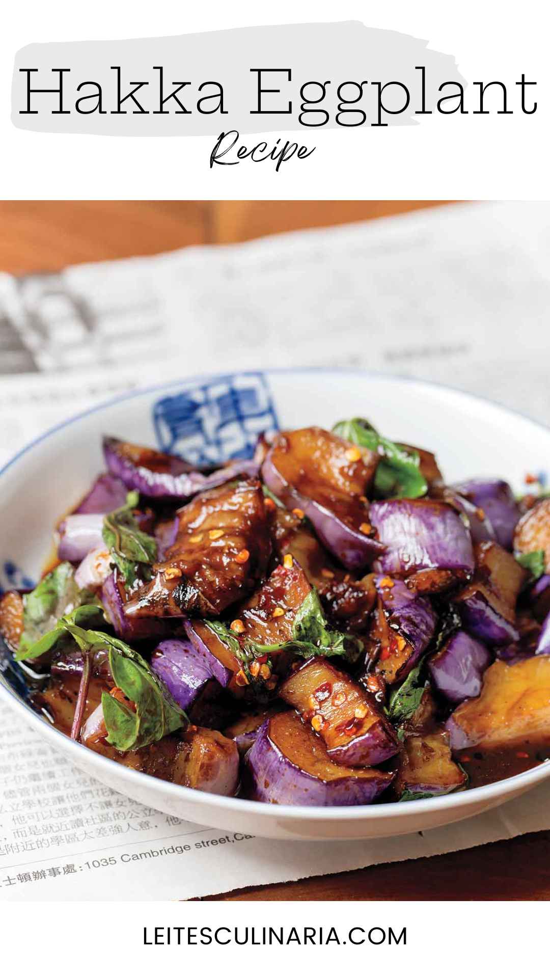 A white bowl filled with stir-fried eggplant in hakka sauce with fresh basil leaves.