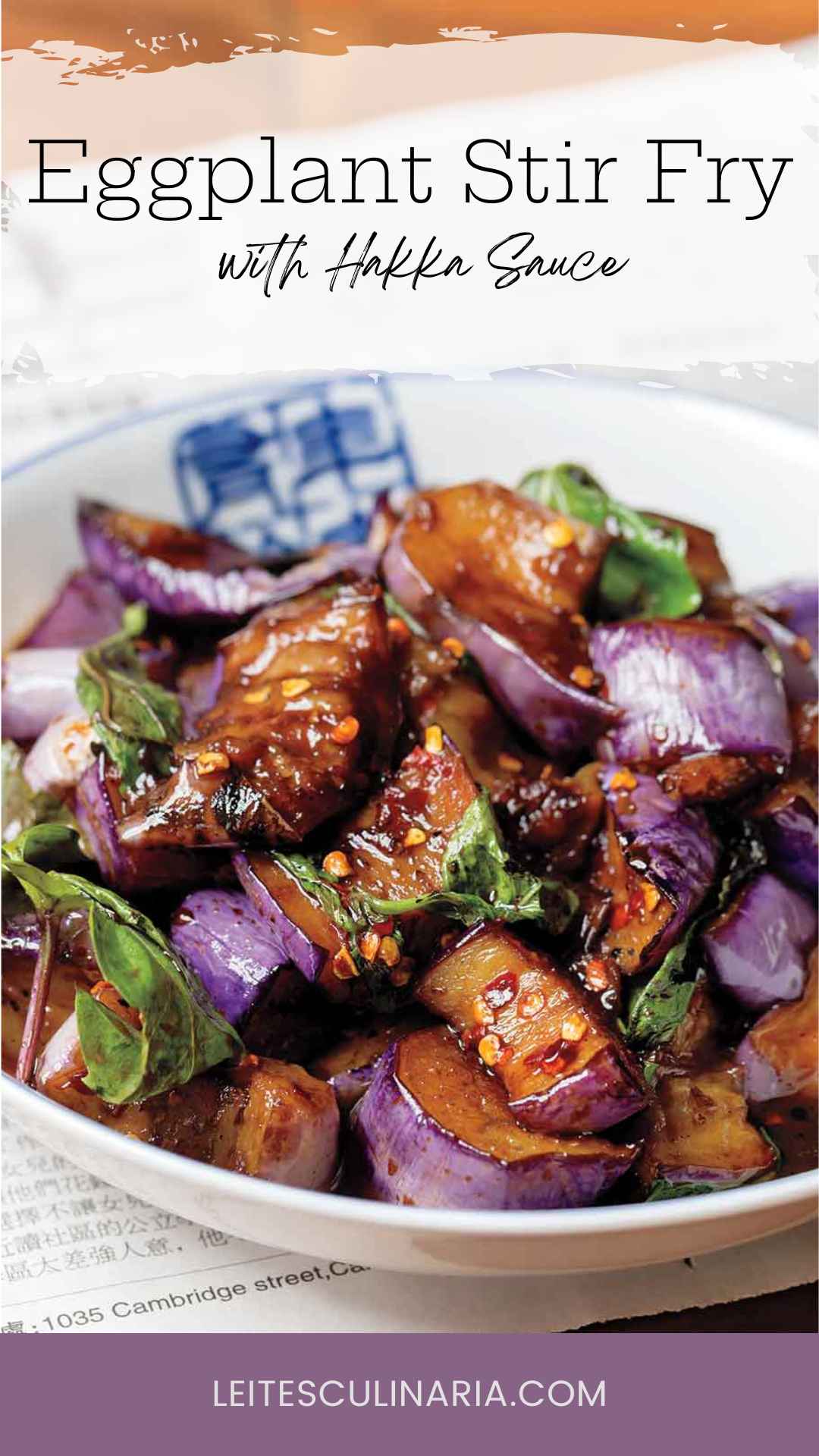 A white bowl filled with stir-fried eggplant in hakka sauce with fresh basil leaves.