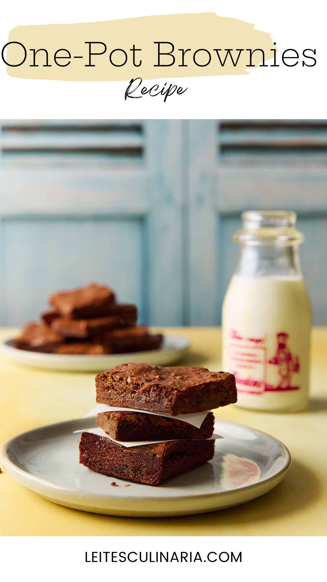 Three brownies stacked on a plate with a bottle of milk in the background.