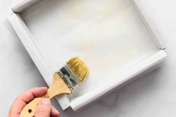 A person brushing butter onto parchment paper in a square cake pan.