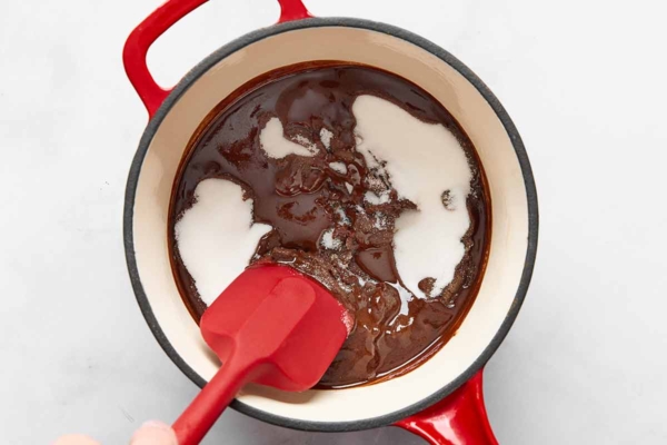 Melted chocolate and sugar being stirred together in a saucepan.