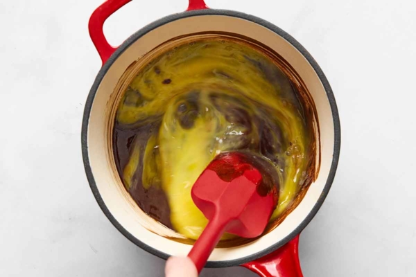 A person stirring beaten egg into a pot of melted chocolate.