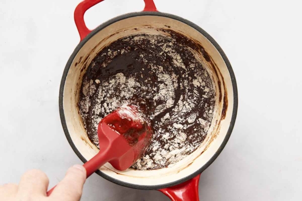 A person stirring flour into chocolate brownie batter in a pot.