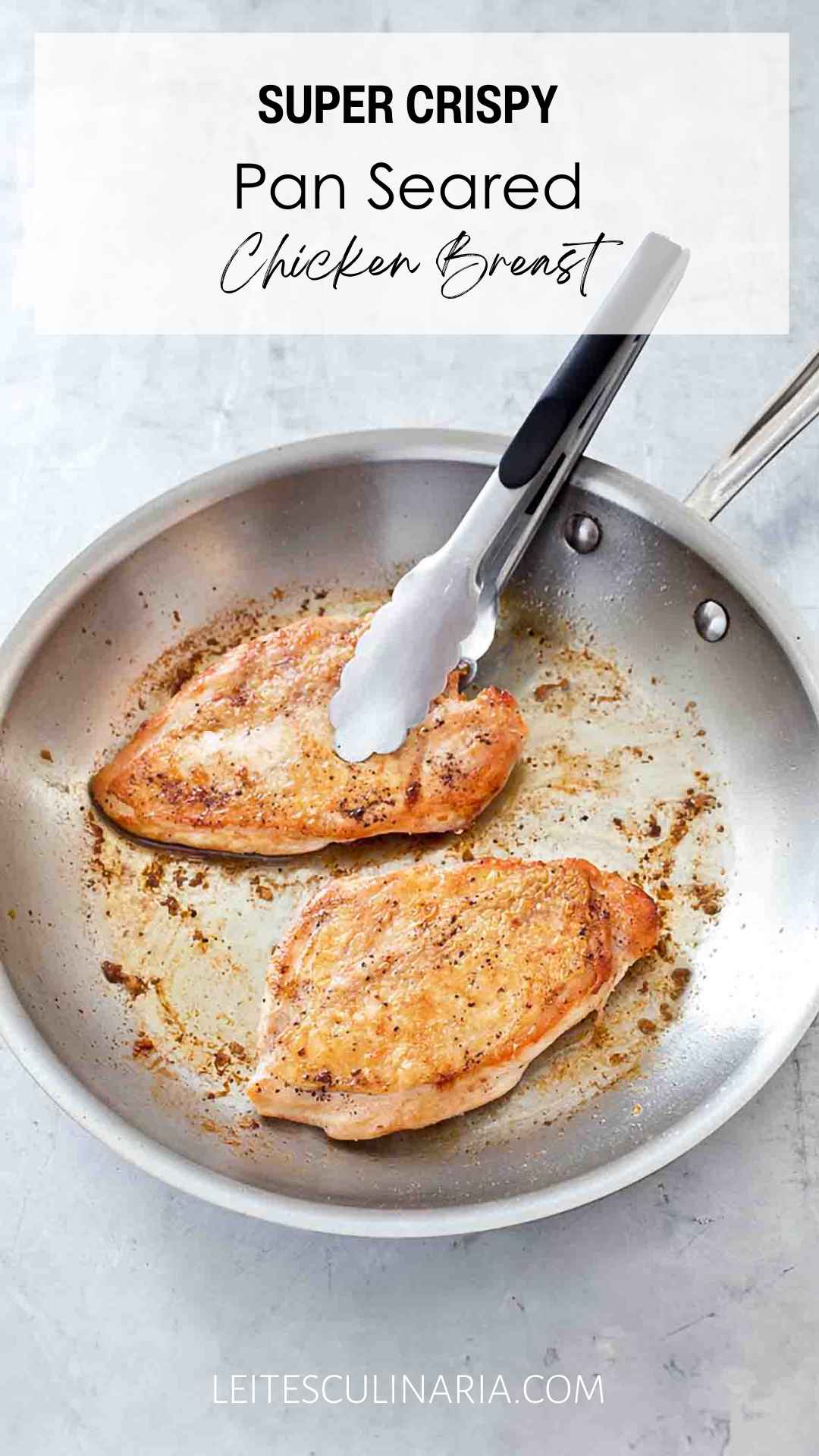 Two crispy pan seared chicken breasts in a metal skillet with a set of tongs.