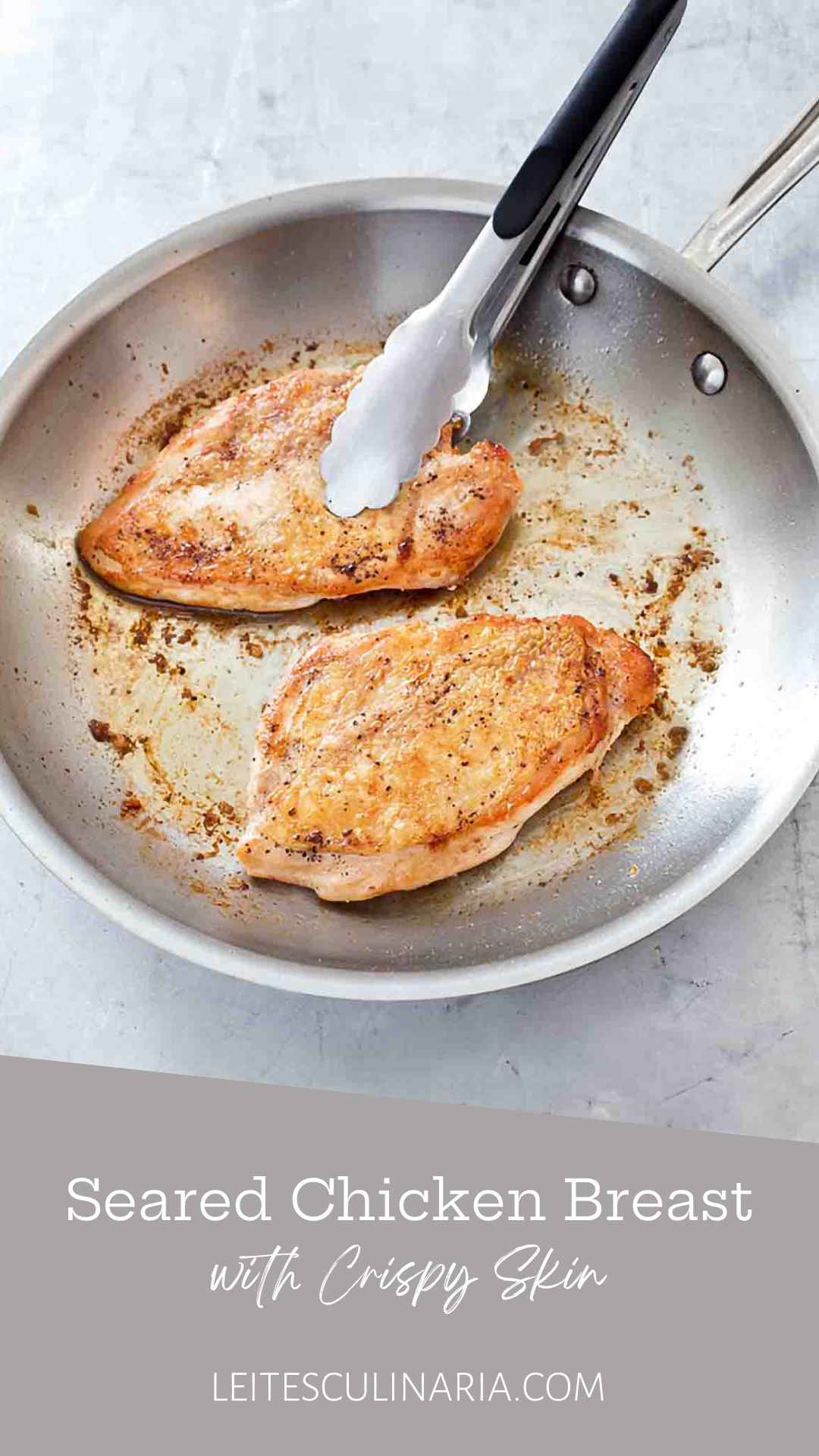 Two crispy pan seared chicken breasts in a metal skillet with a set of tongs.