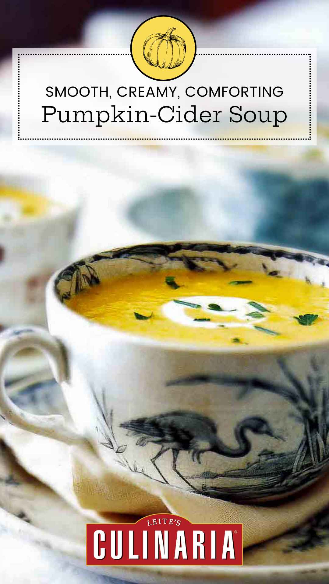 A large teacup filled with pumpkin cider soup with a swirl of creme fraiche and some herbs sprinkled on top.