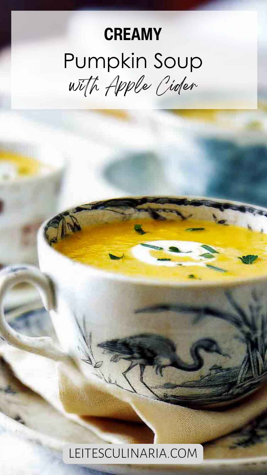 A large teacup filled with pumpkin cider soup with a swirl of creme fraiche and some herbs sprinkled on top.