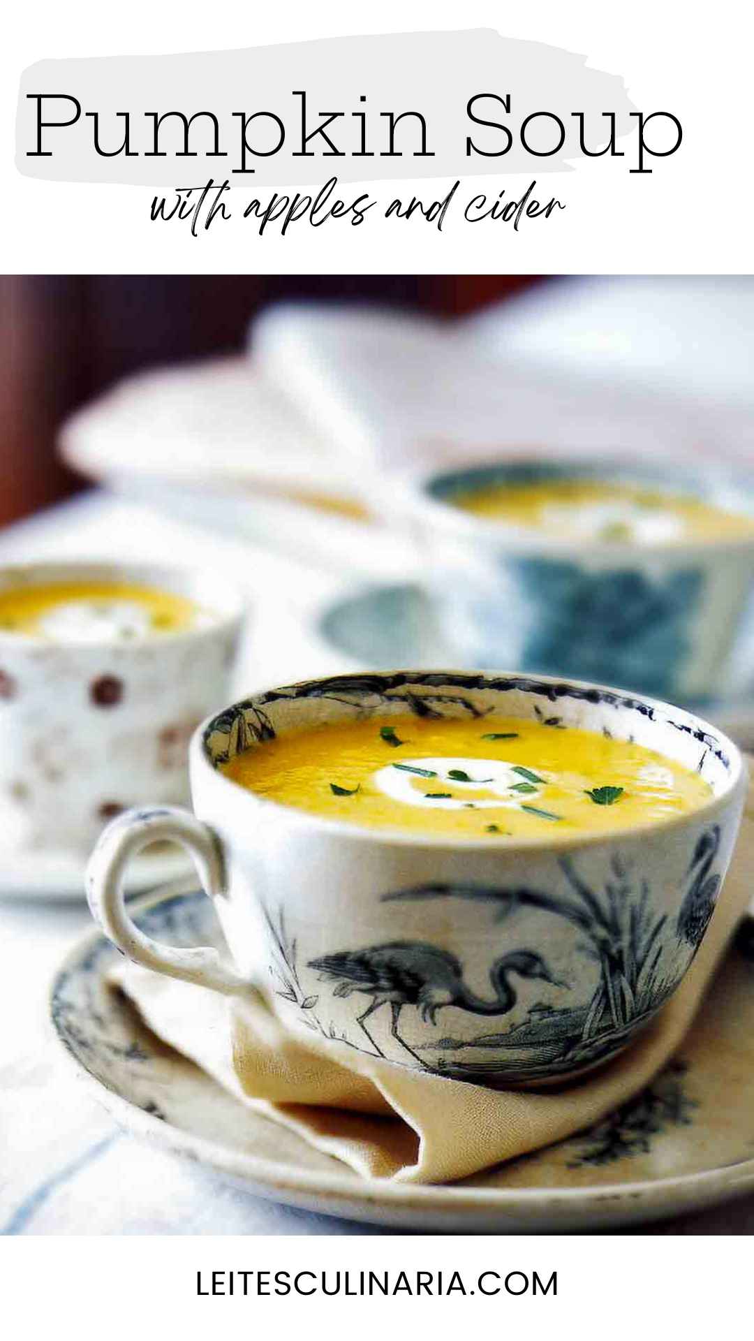 A large teacup filled with pumpkin cider soup with a swirl of creme fraiche and some herbs sprinkled on top.