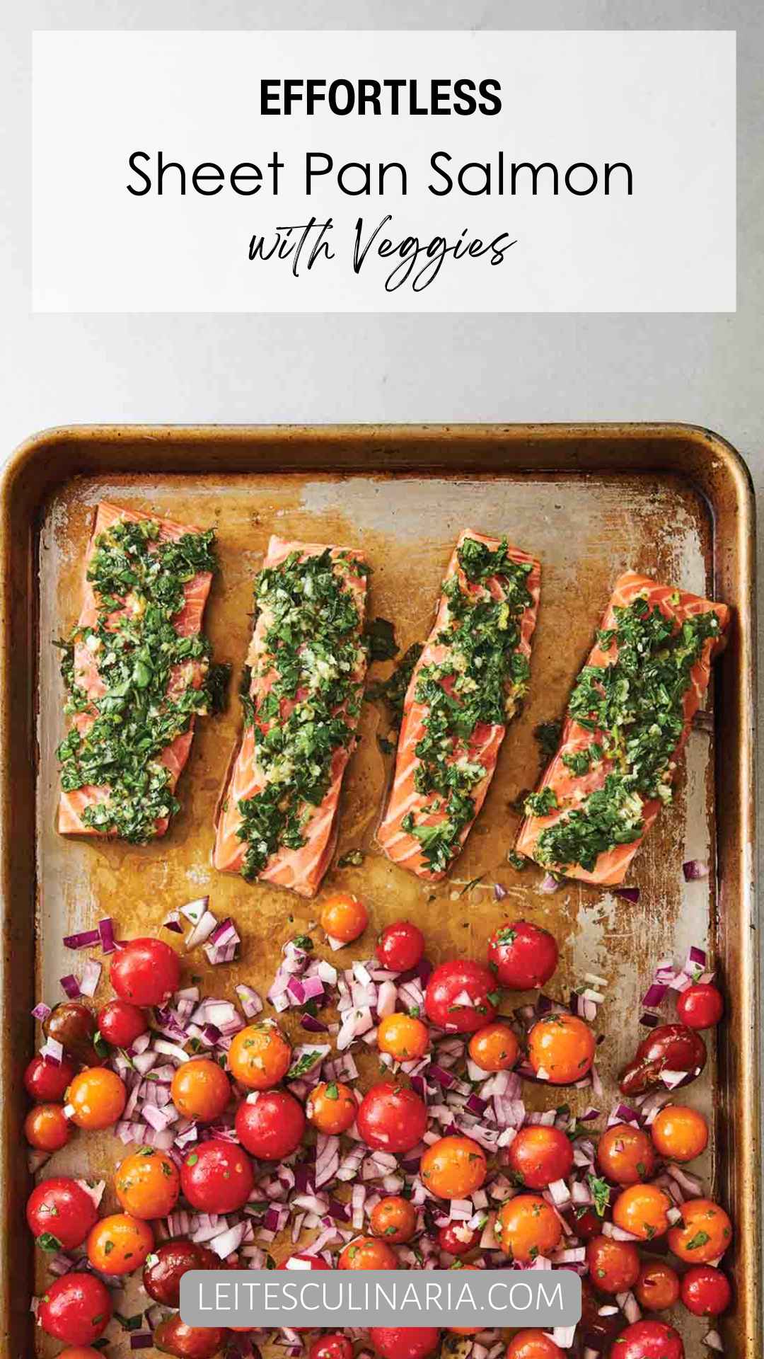 A baking sheet with four filets of salmon topped with a herb mixture, and a mixture of cherry tomatoes and red onion on the rest of the sheet.