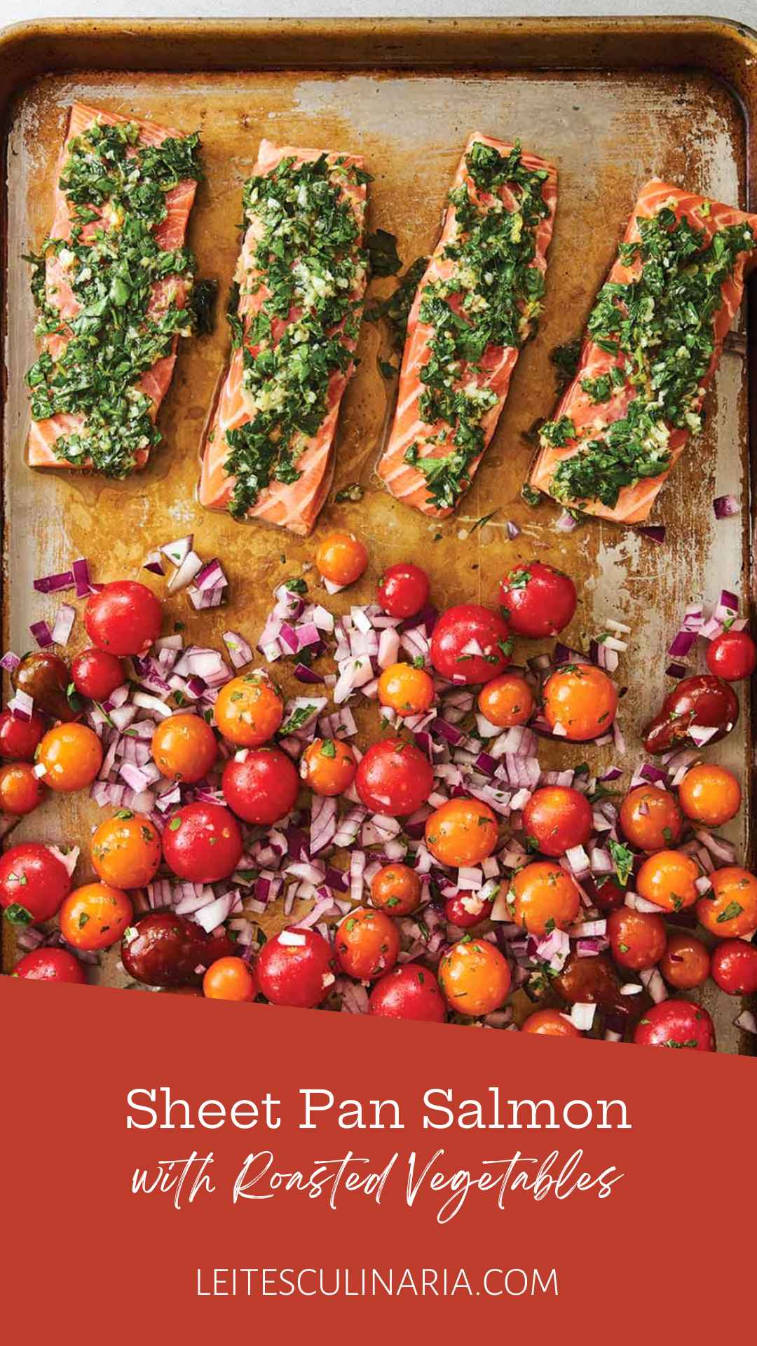 A baking sheet with four filets of salmon topped with a herb mixture, and a mixture of cherry tomatoes and red onion on the rest of the sheet.