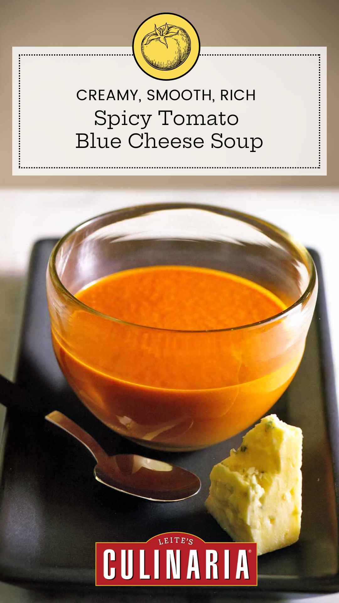 A bowl of tomato soup with a spoon and a wedge of blue cheese on the side.