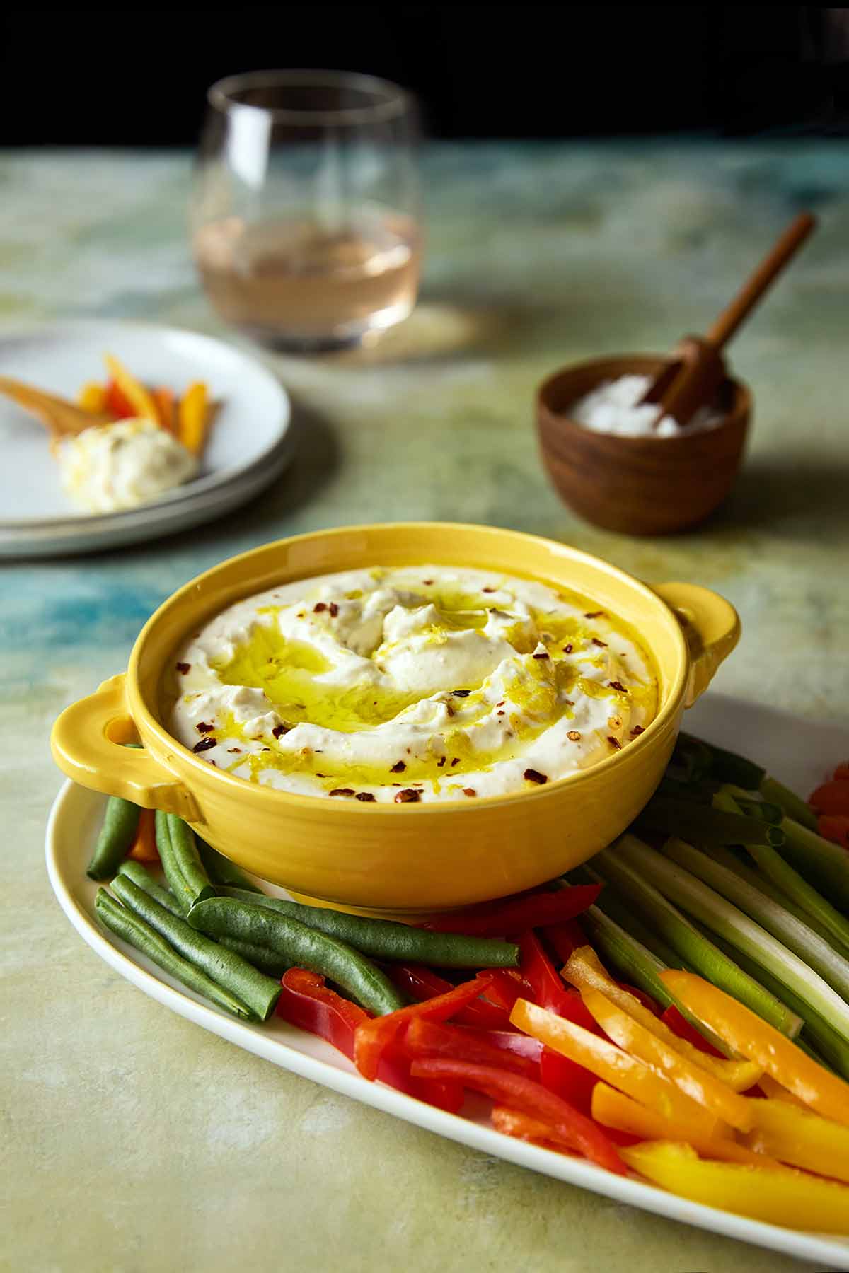 A bowl of whipped feta dip topped with oil and lemon zest on a platter of raw vegetables.