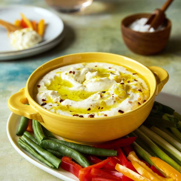 A bowl of whipped feta dip topped with oil and lemon zest on a platter of raw vegetables.