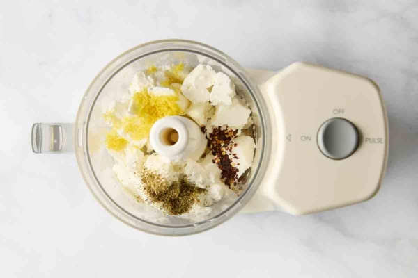 Feta, lemon, and spices combined in the bowl of a food processor.